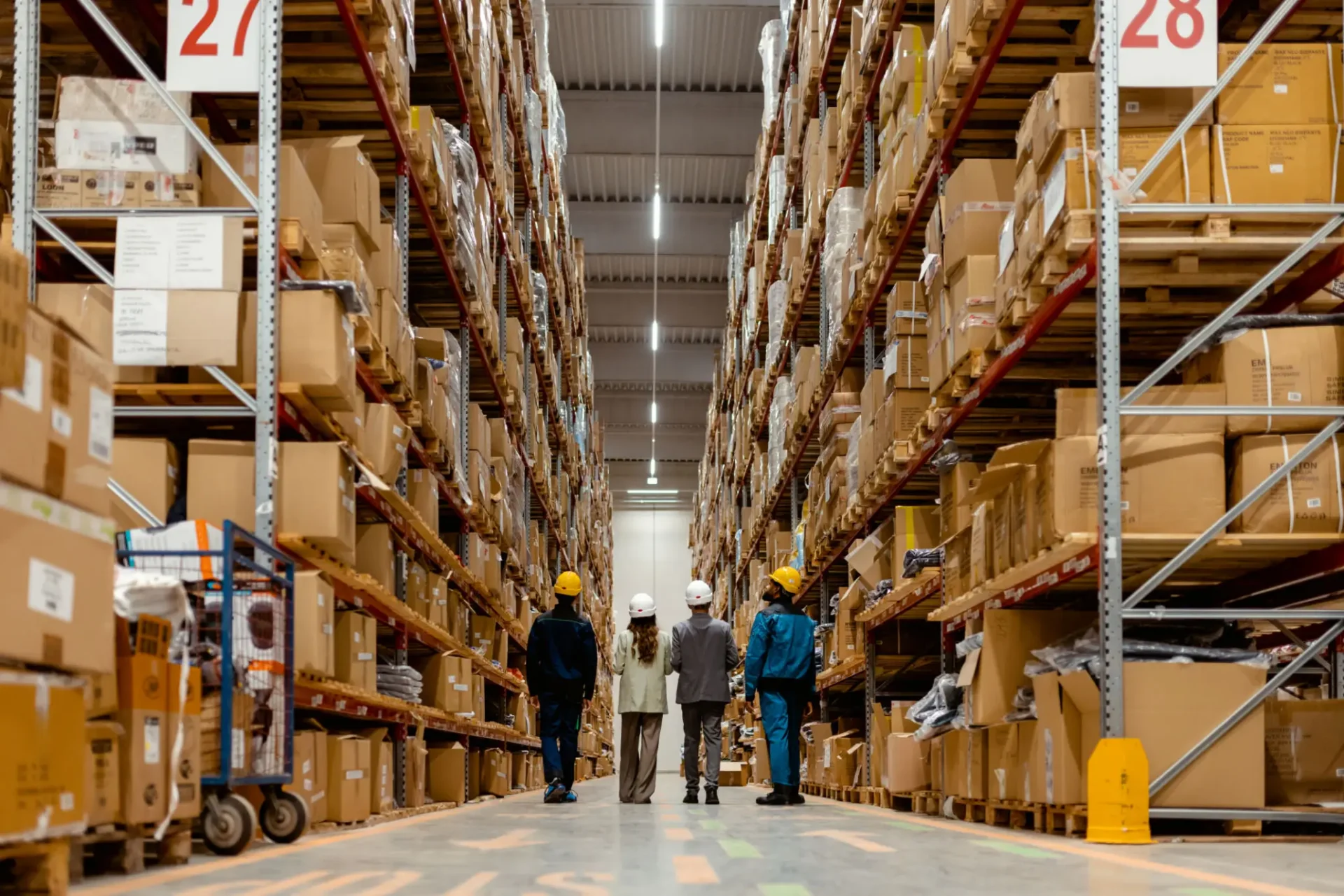 Four workers in hard hats walking warehouse aisle